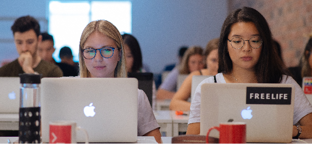 Two women typing in Macbooks