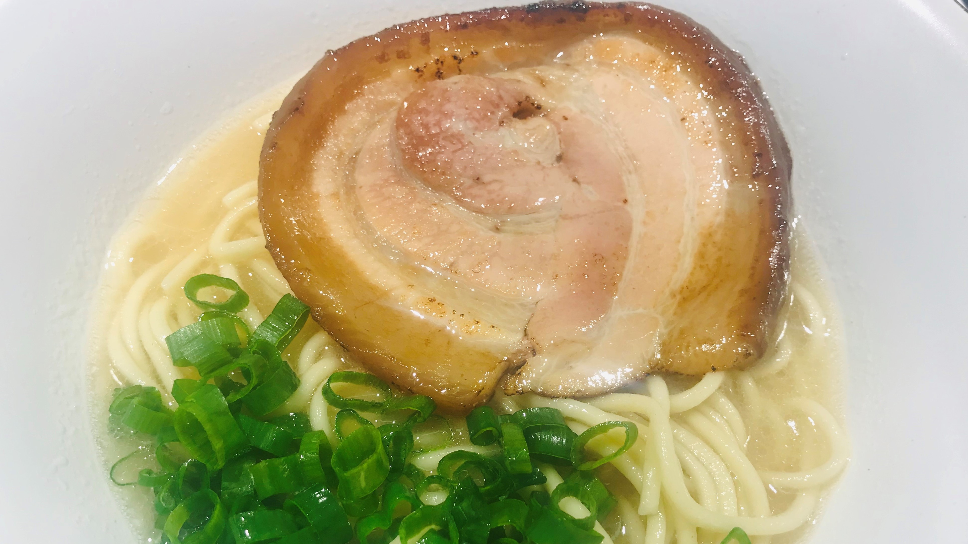 Top view of a bowl of ramen with pork belly, scallions, and noodles